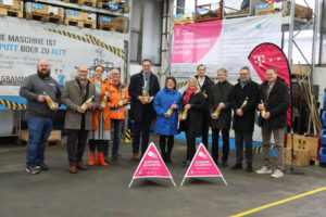 Pressetermin zum Glasfaserausbau in Denkendorf: Vertreter von Telekom, Kommune und Region stehen in einer Industriehalle vor Glasfaser-Banner und Baustellenschildern.